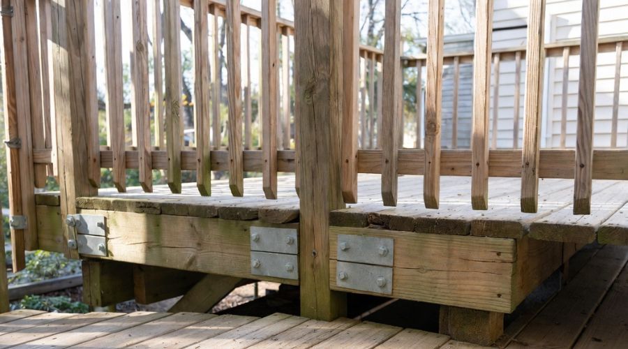 Wooden deck framing showing two beams joined at a post using metal structural plates and large through-bolts.