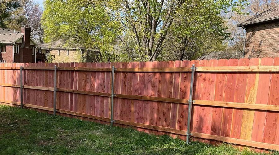 Red wooden fence enclosing a grassy backyard with trees and houses in the background