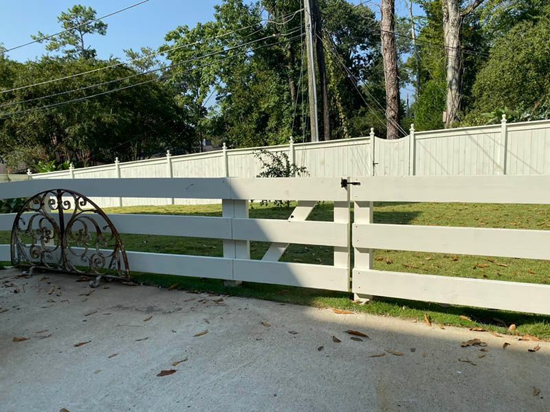 A white fence surrounds a yard with trees in the background