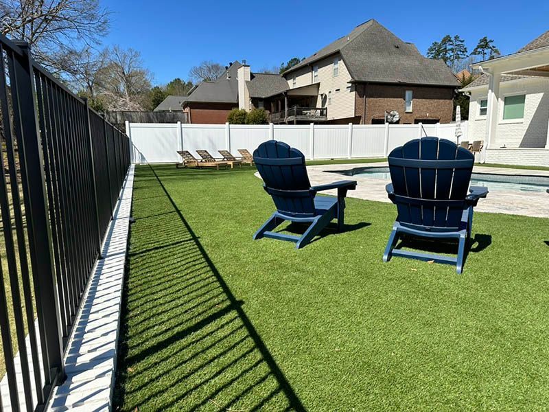 Two chairs are sitting on a lush green lawn next to a pool.