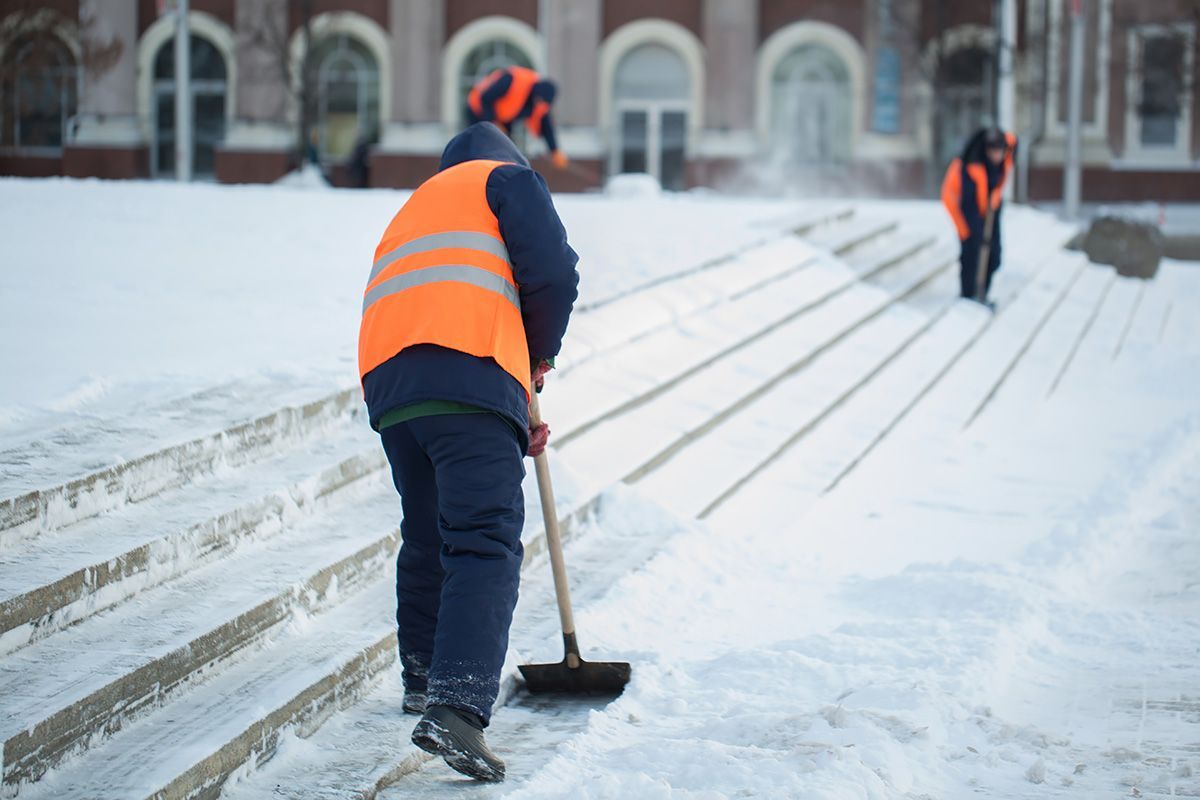 A man is sweeping snow from the sidewalk with a broom.