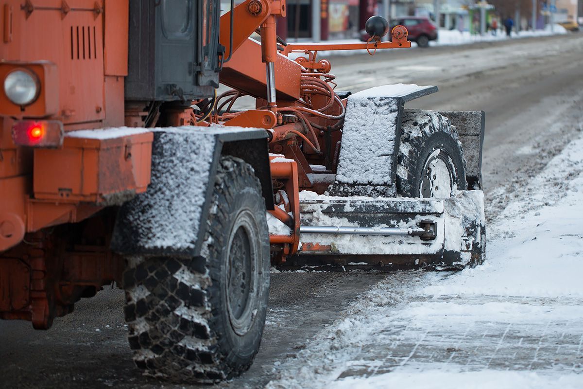 An orange tractor is clearing snow from the side of the road.