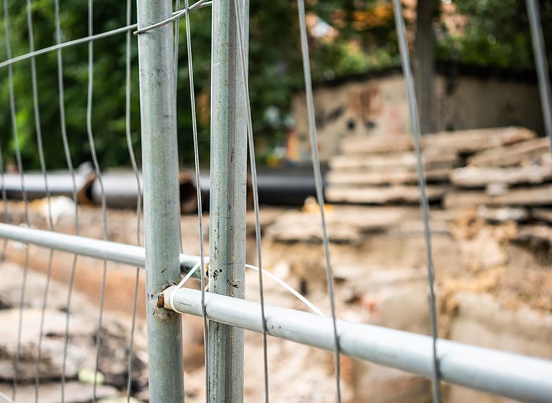 A close up of a metal fence with a pile of wood in the background.