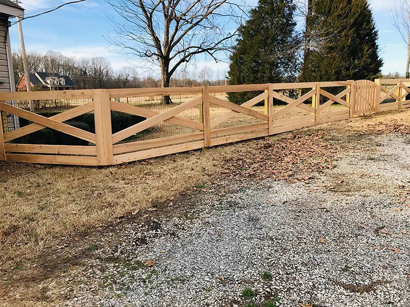 A wooden fence is sitting on the side of a gravel road.