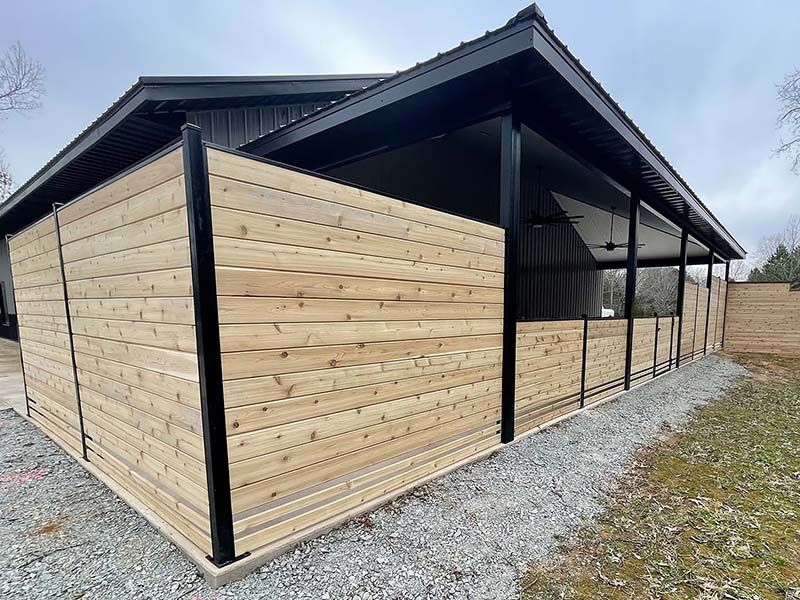 A wooden fence surrounds a building with a black roof.