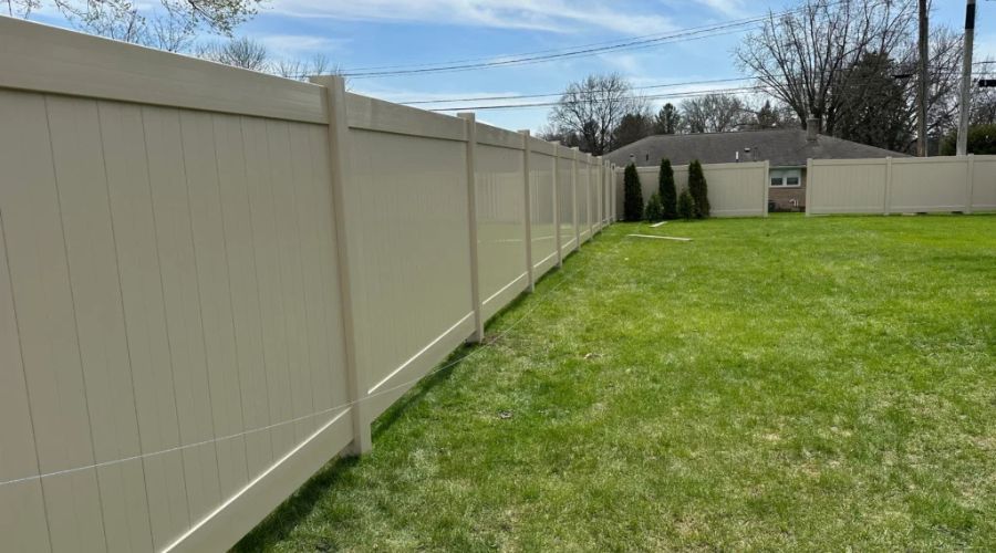 Beige vinyl privacy fence enclosing a residential lawn