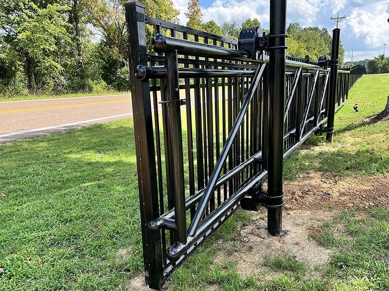 A black metal fence is sitting in the grass next to a road.