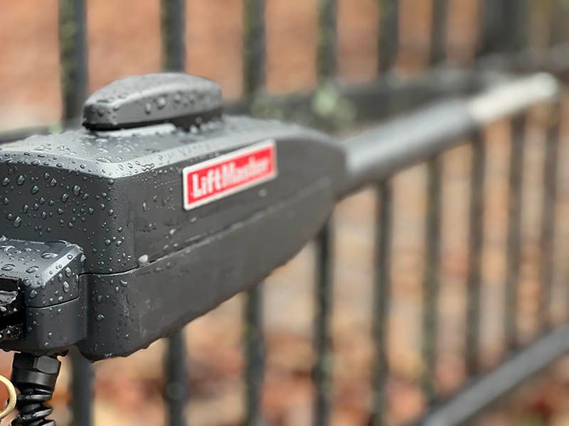 A close up of a lift master gate opener on a fence.