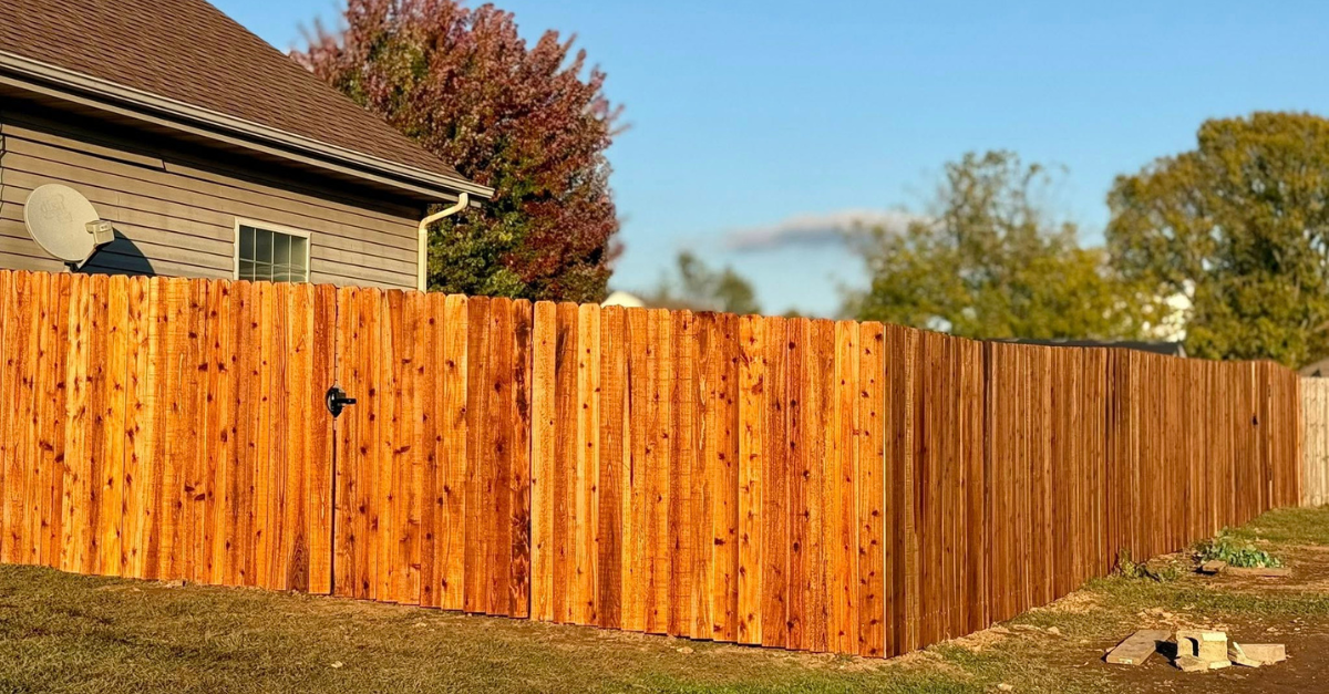 Wooden fence surrounding a house with a green lawn and autumn trees.