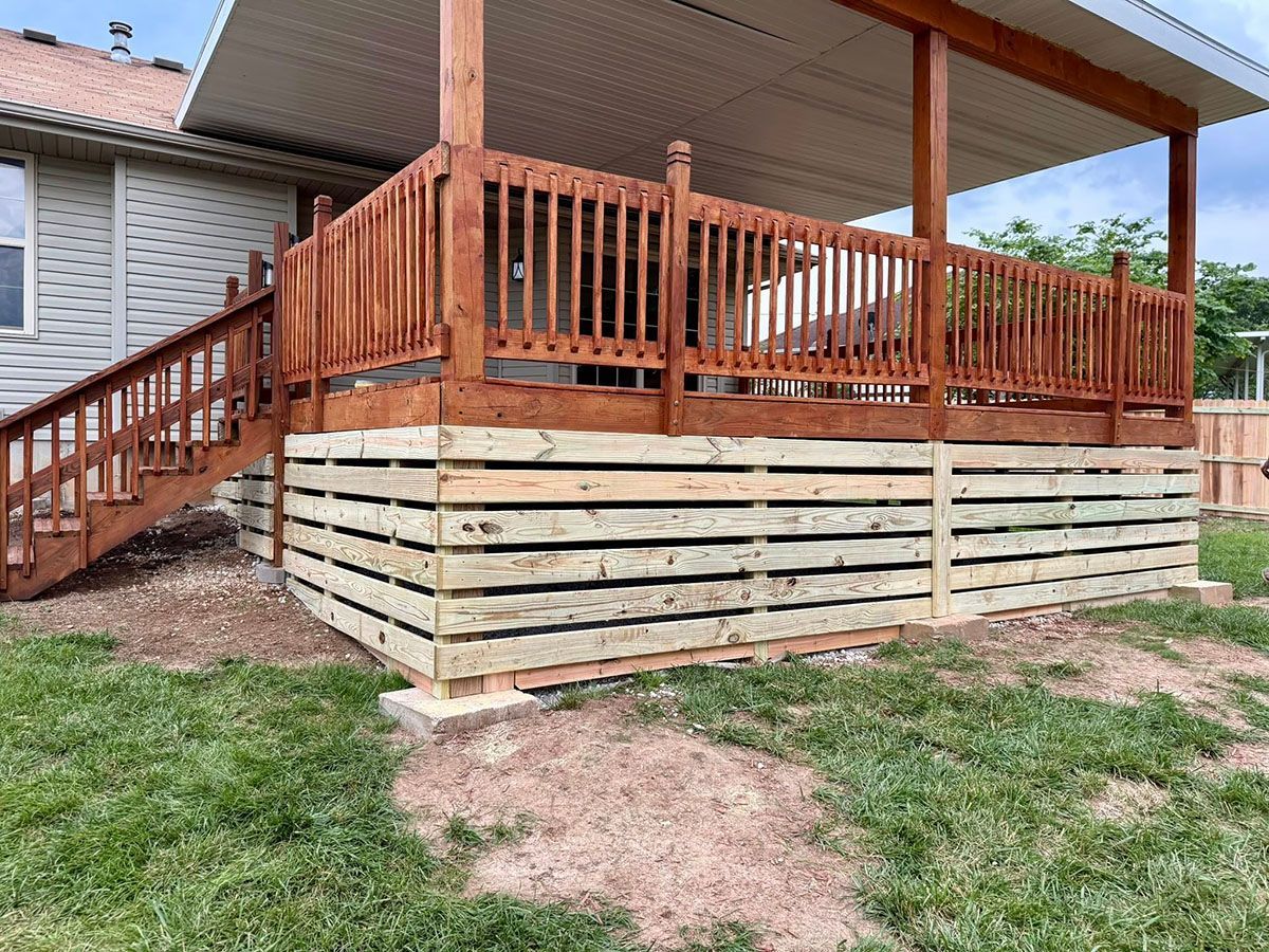 A wooden deck with stairs leading up to it is in the backyard of a house.