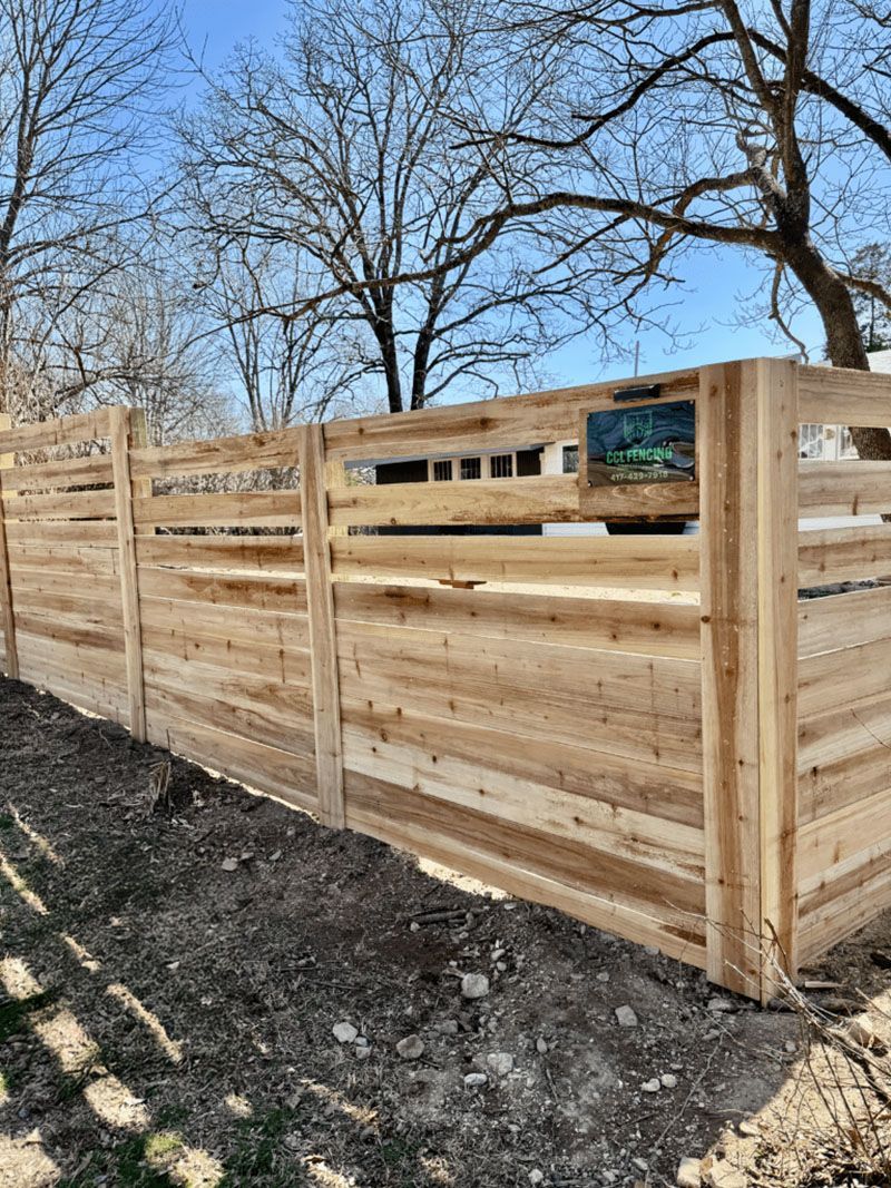 A wooden fence is surrounded by trees in a yard.