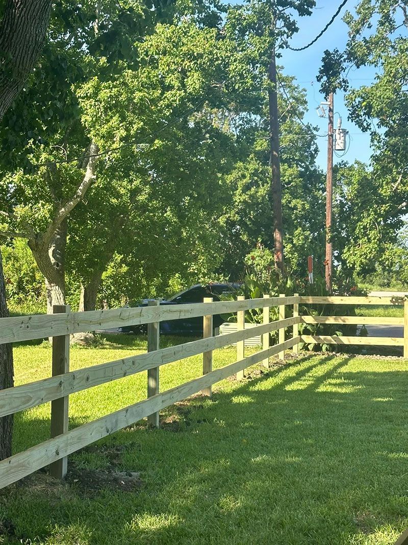 A wooden fence surrounds a grassy field with trees in the background.