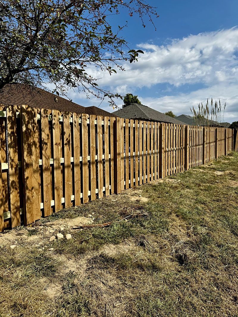 A wooden fence surrounds a grassy field in front of a house.
