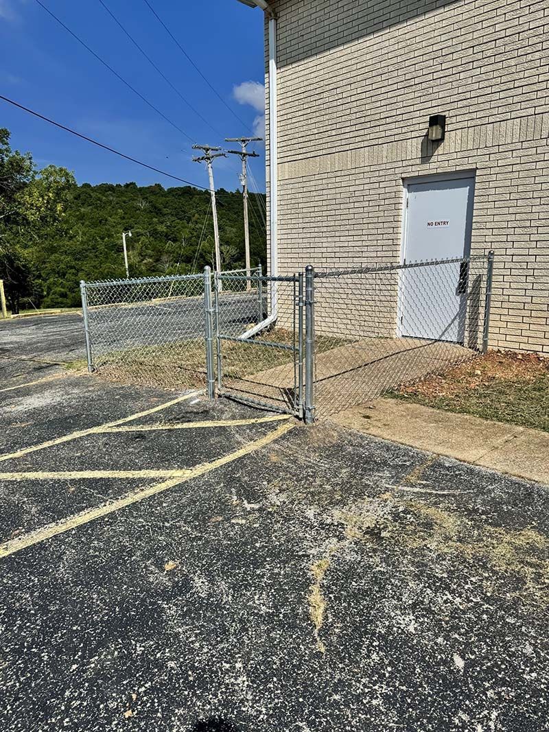 A chain link fence is surrounding a parking lot next to a building.