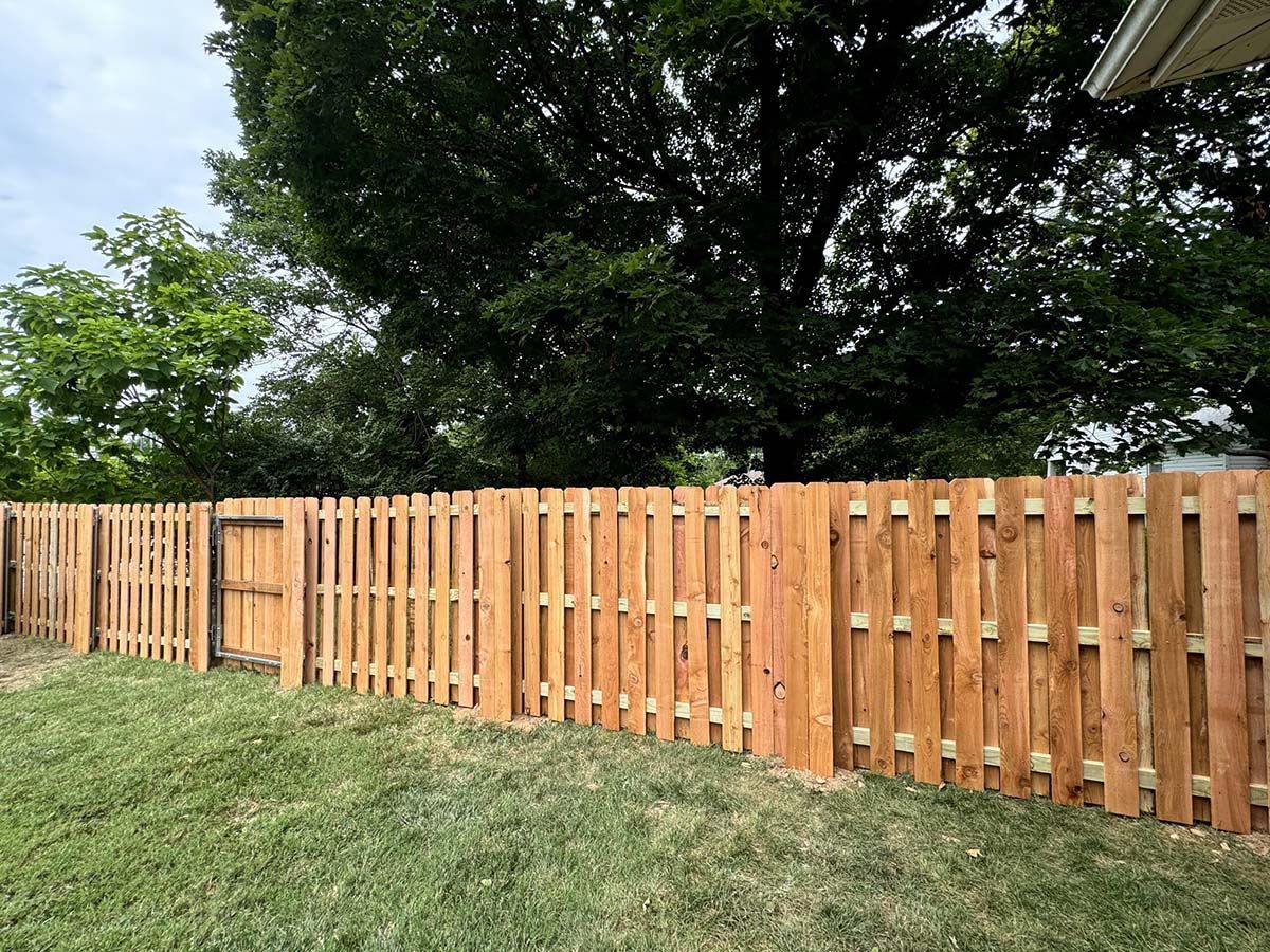 A wooden fence in a backyard with trees in the background.
