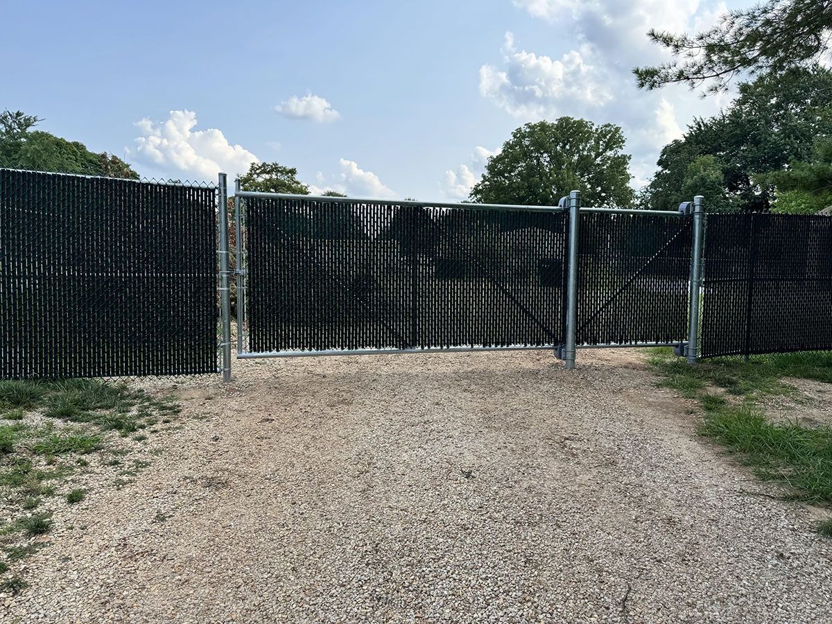 A black fence is surrounding a gravel road.