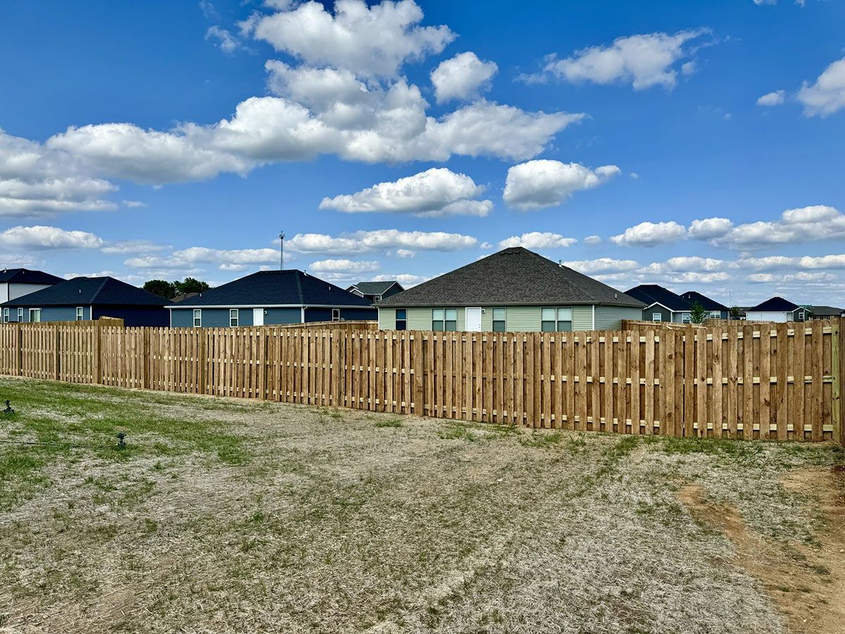 A wooden fence surrounds a residential area with houses in the background.