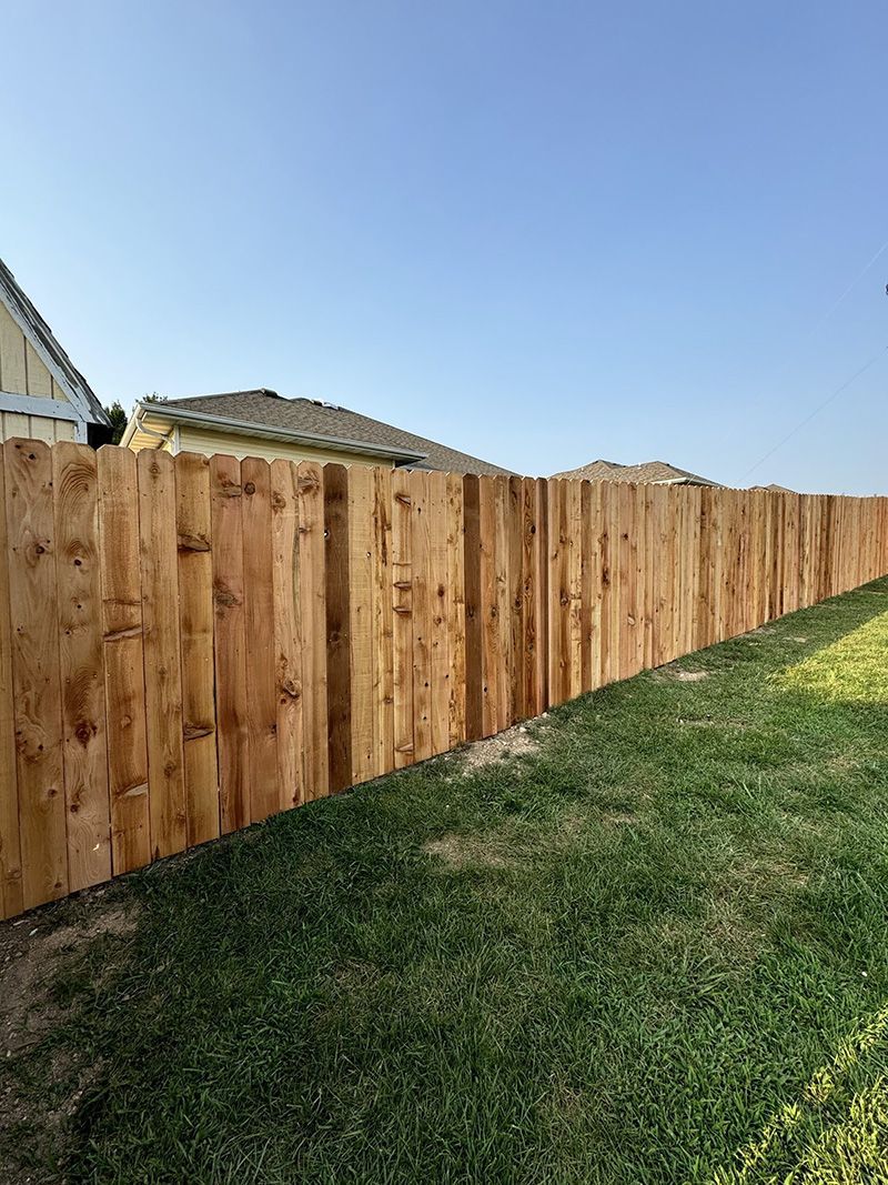 A wooden fence is sitting on top of a lush green lawn next to a house.