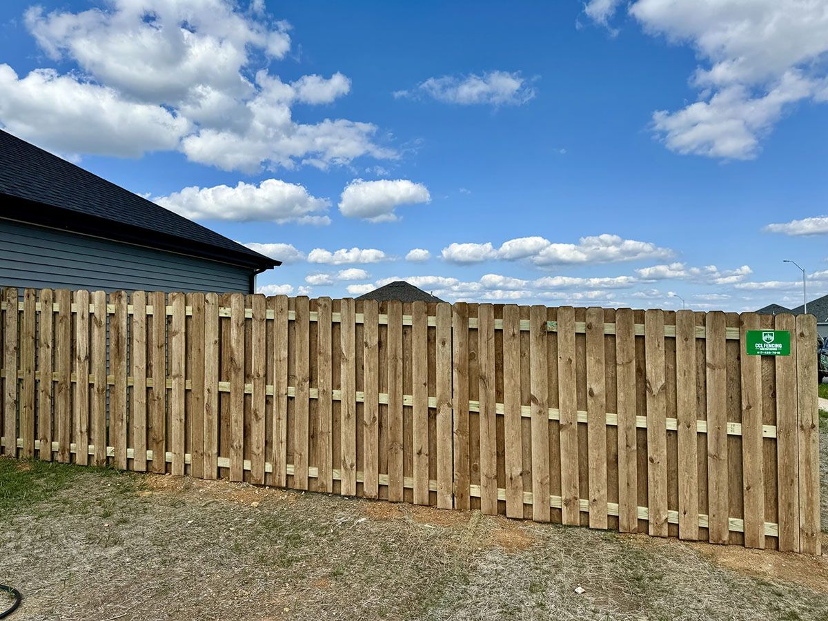 A wooden fence in front of a house with a blue sky in the background.