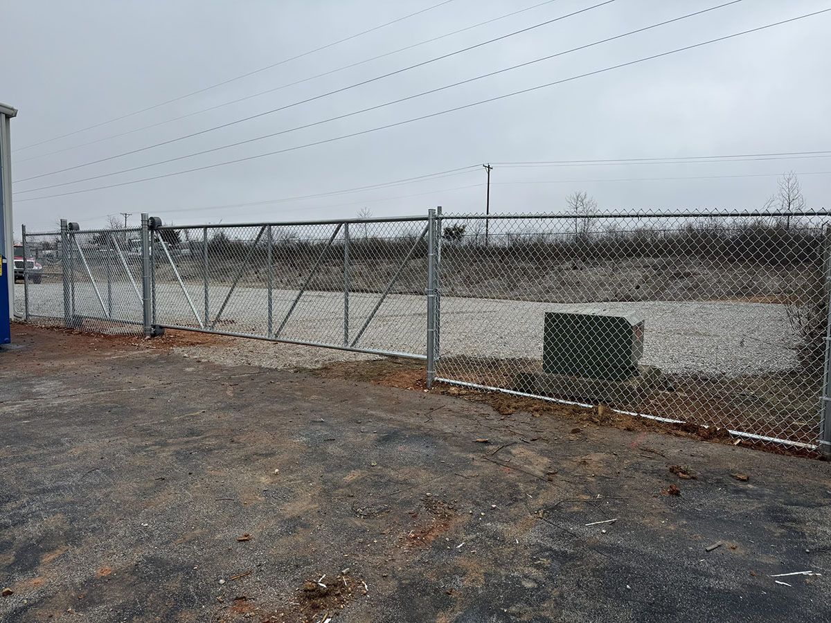 A chain link fence with a gate in the middle of a dirt field.