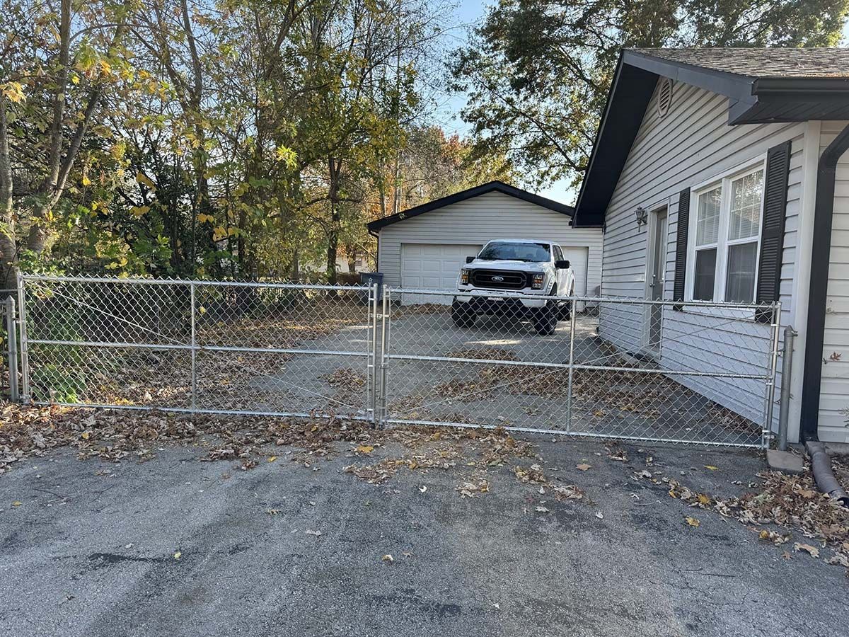 A white truck is parked in front of a white house behind a chain link fence.