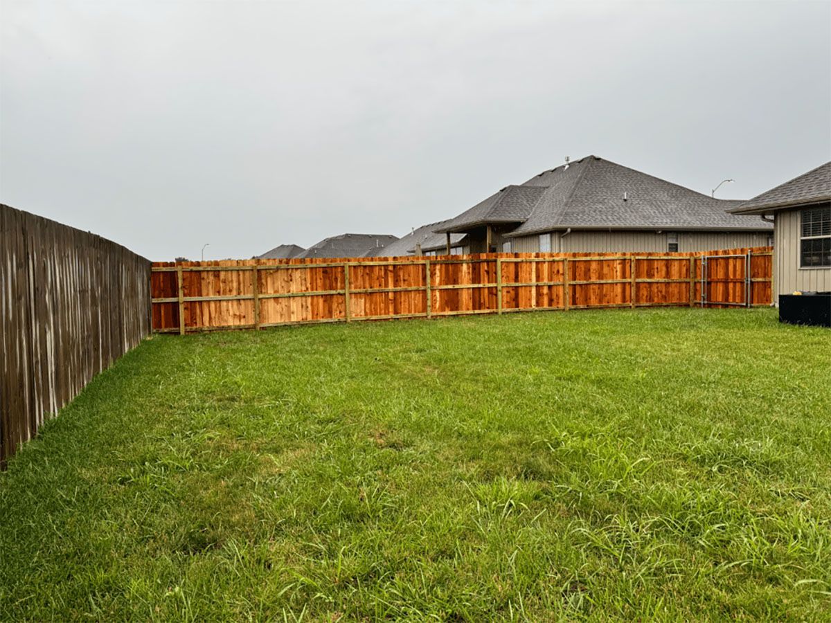 A backyard with a wooden fence and a house in the background.