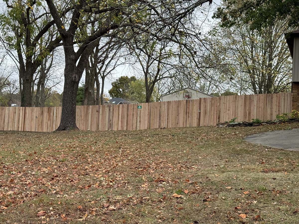 A wooden fence is surrounded by trees and leaves in a yard.