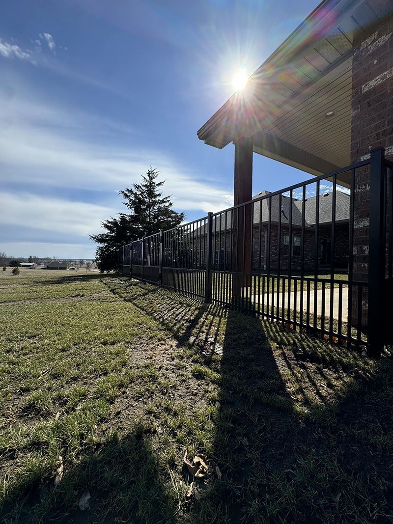 The sun is shining through the fence and casting a shadow on the grass.