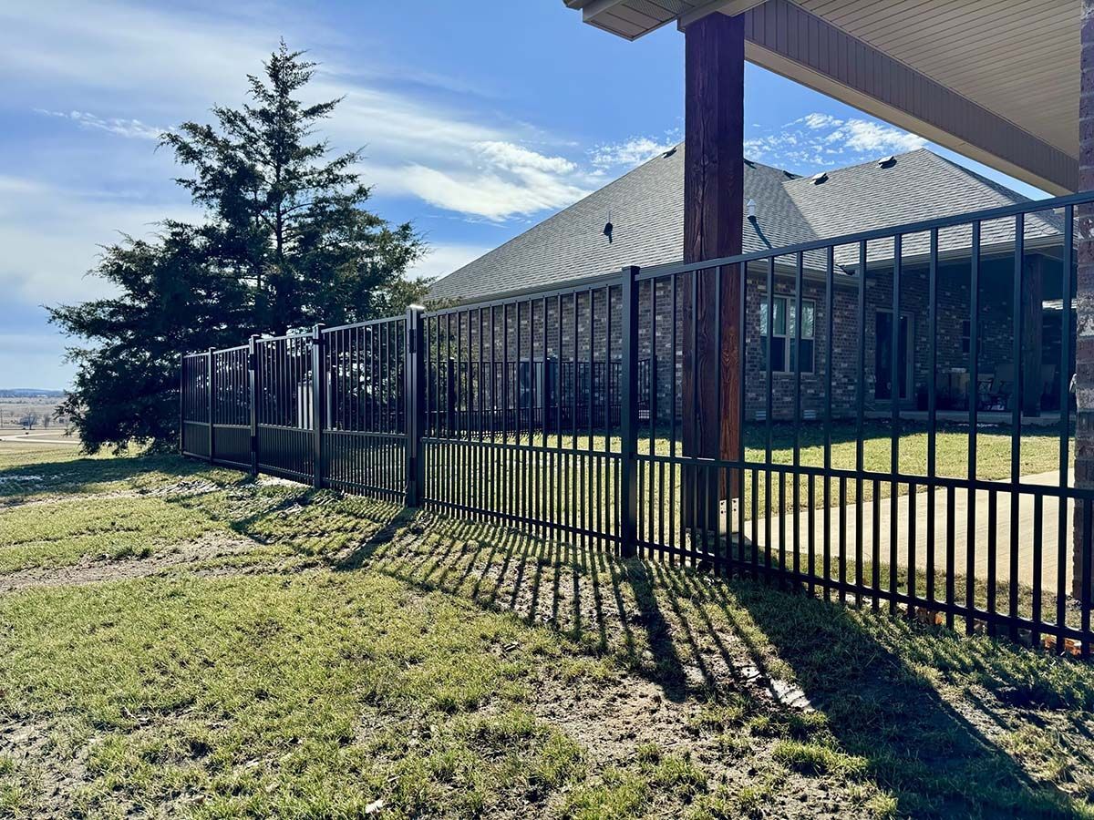 A metal fence is surrounding a brick house in a grassy yard.