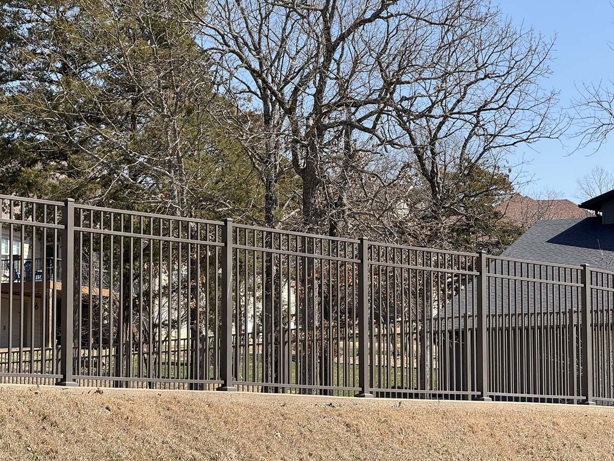 A metal fence with trees in the background and a house in the background.