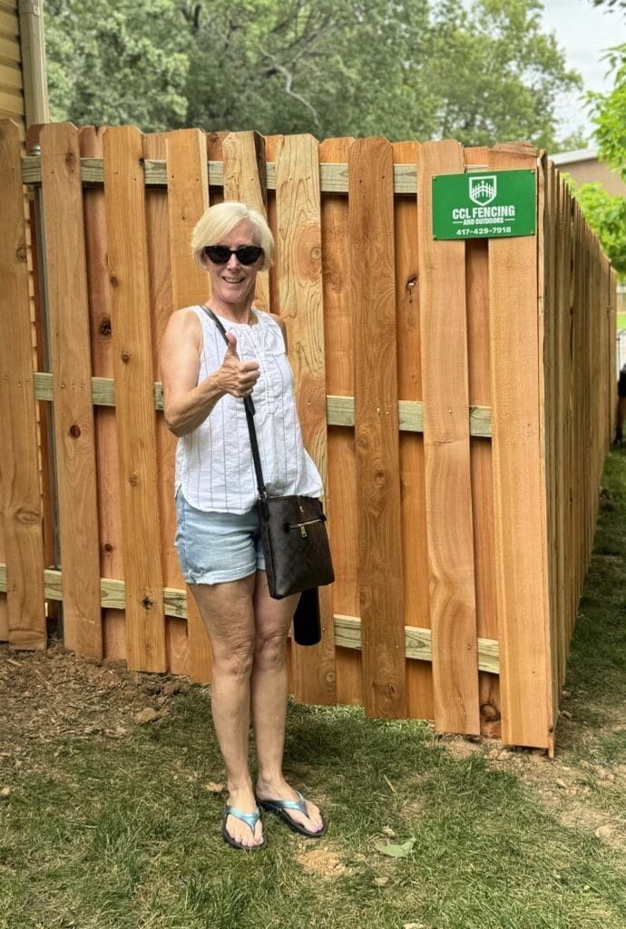 A woman is standing in front of a wooden fence.
