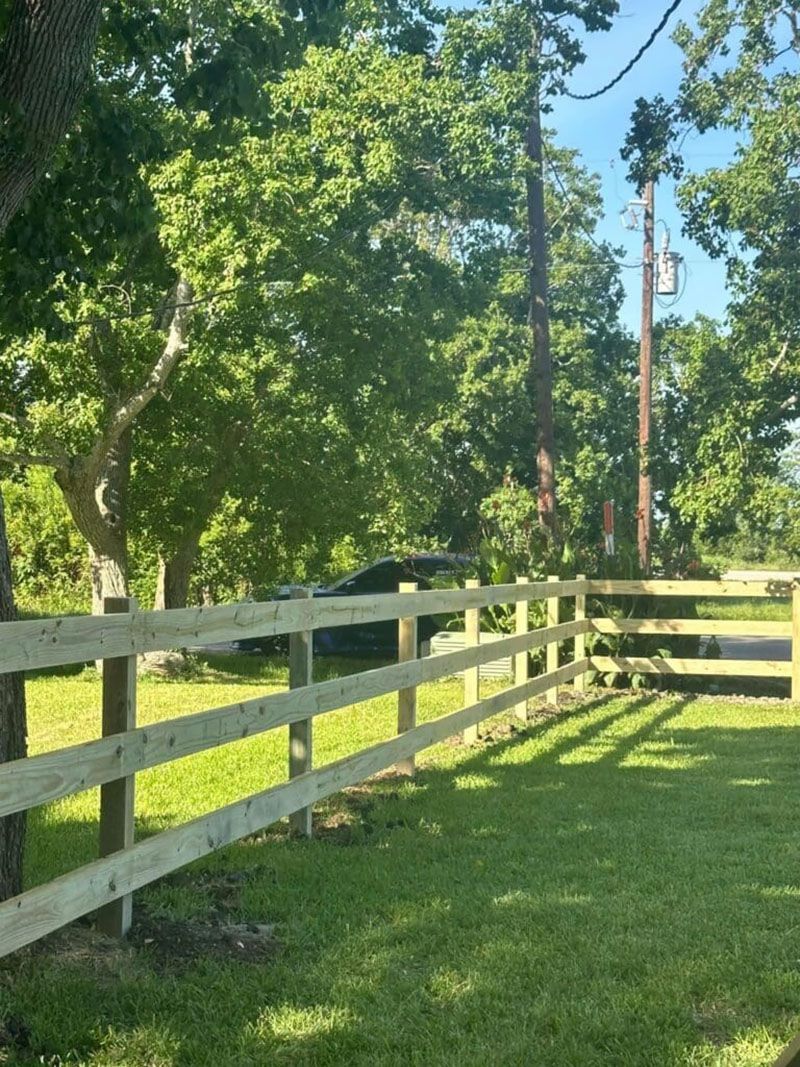 A wooden fence surrounds a grassy field with trees in the background.