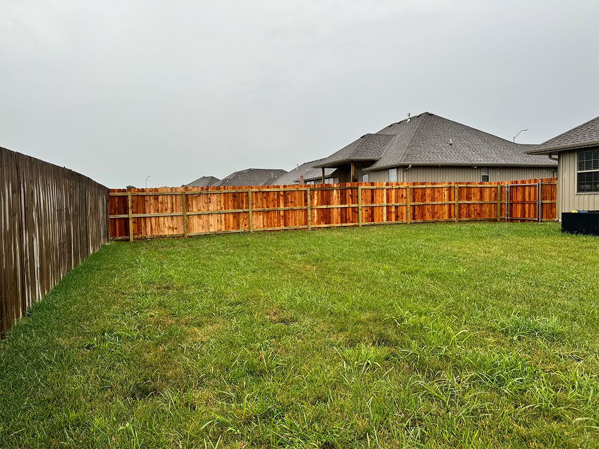 A backyard with a wooden fence and a house in the background.