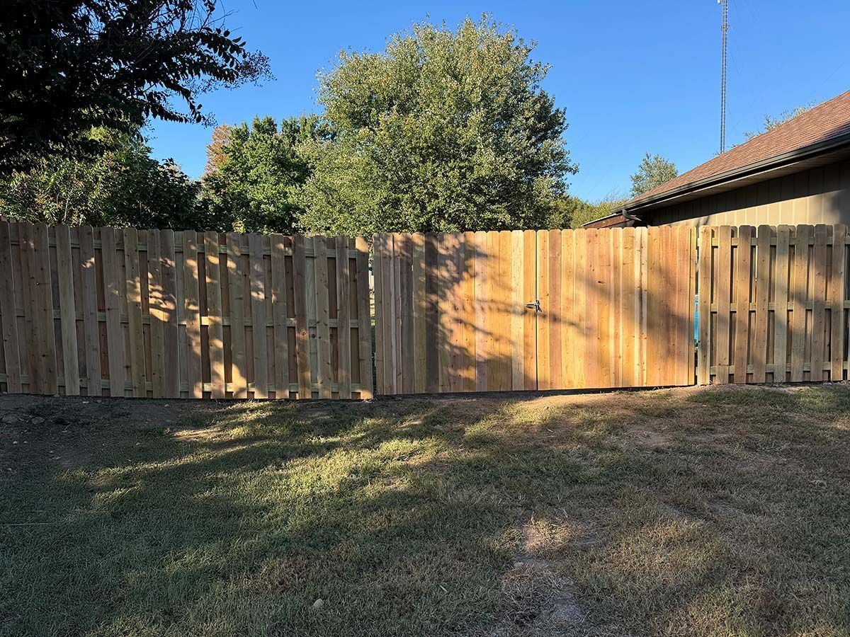 A wooden fence surrounds a grassy yard in front of a house.