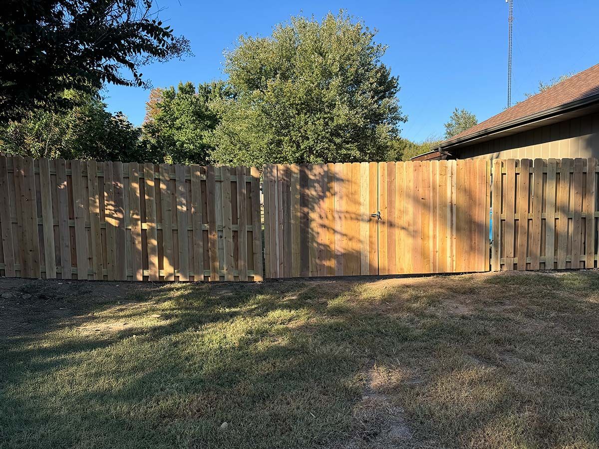 A wooden fence surrounds a grassy yard in front of a house.
