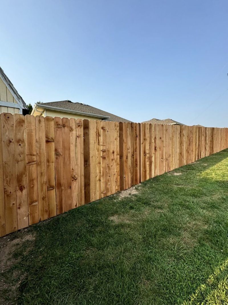 A wooden fence is sitting on top of a lush green lawn next to a house.