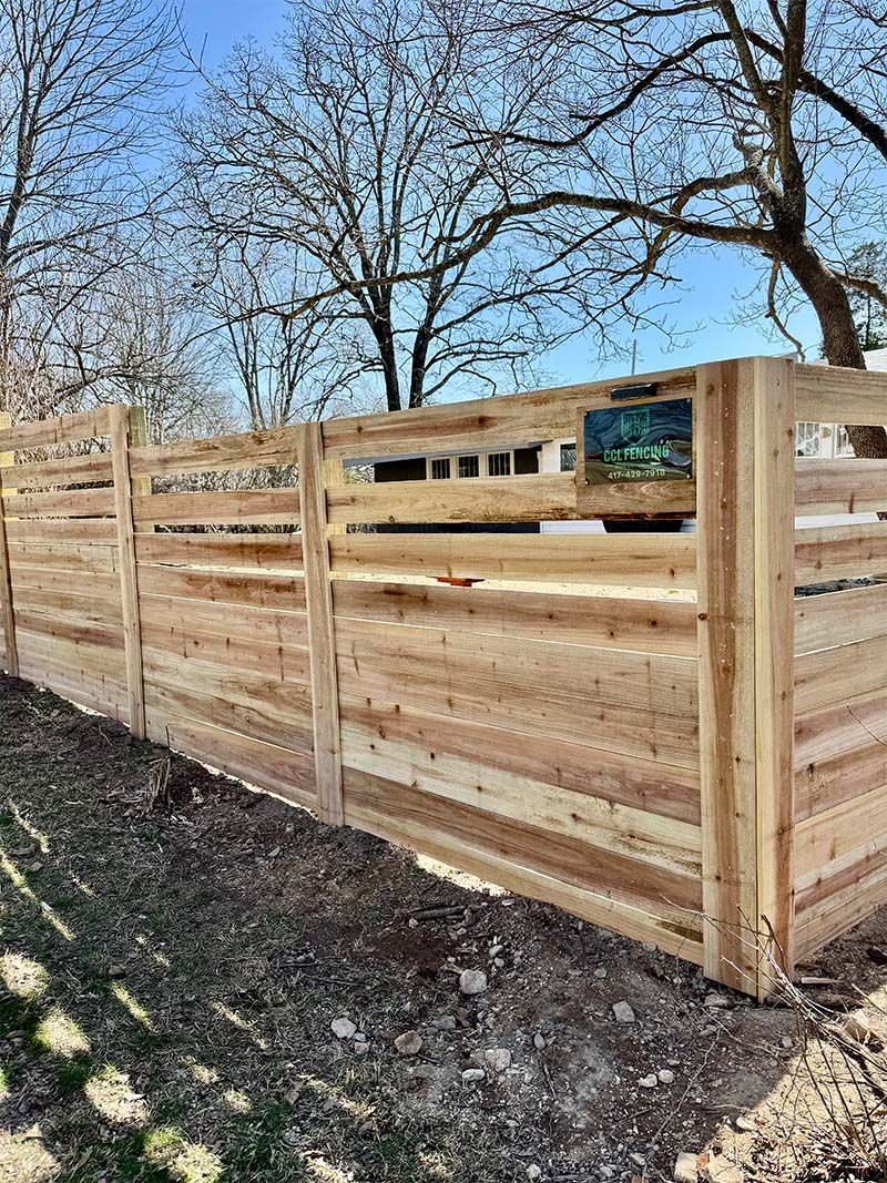 A wooden fence with trees in the background and a blue sky in the background.