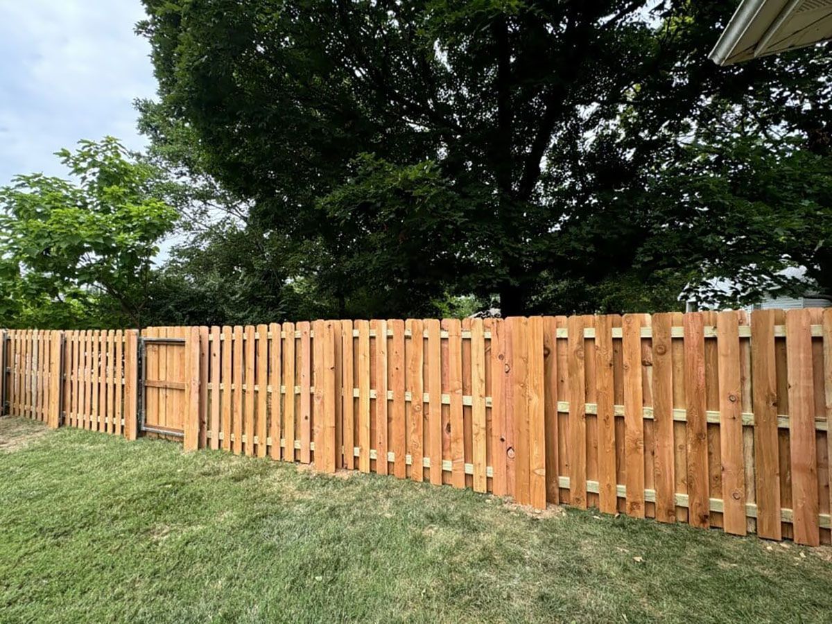 A wooden fence in a backyard with trees in the background.