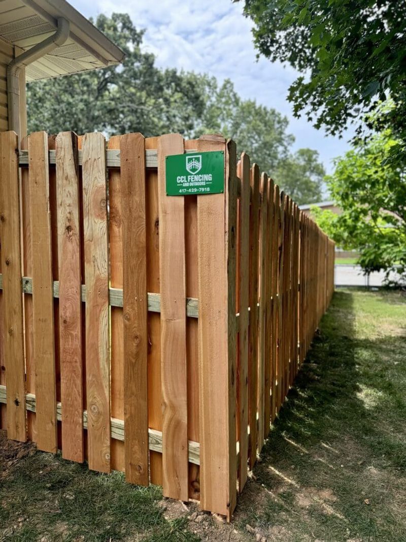 A wooden fence with a green sign on it is next to a house.
