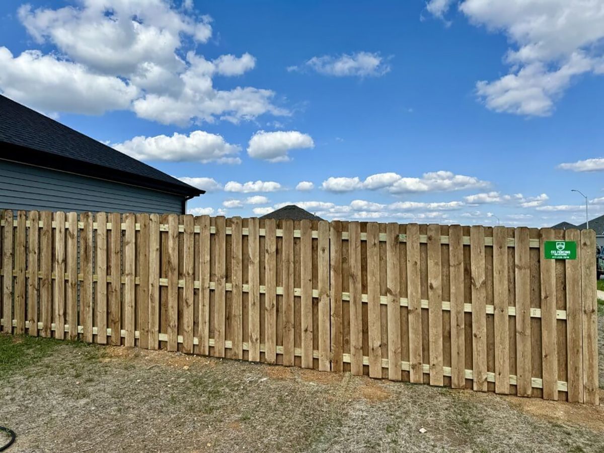 A wooden fence in front of a house with a blue sky in the background.