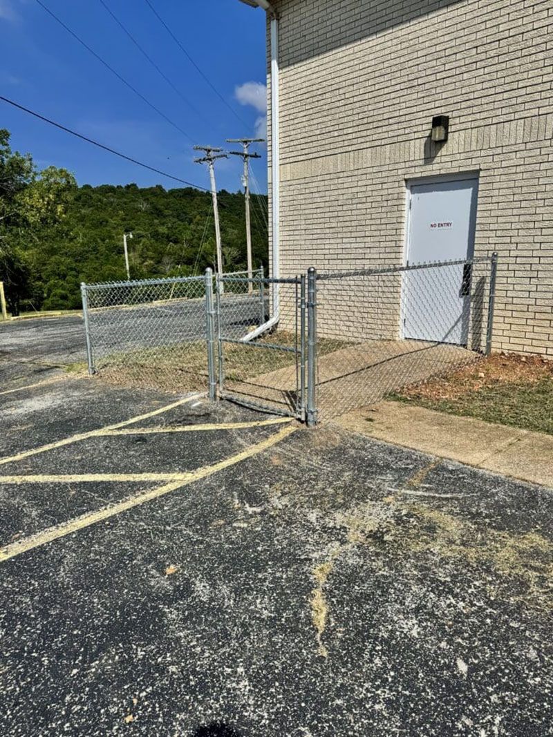 A chain link fence is surrounding a parking lot next to a building.