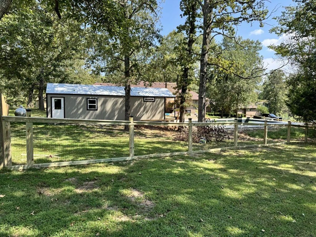 A small house with a wooden fence in front of it surrounded by trees.