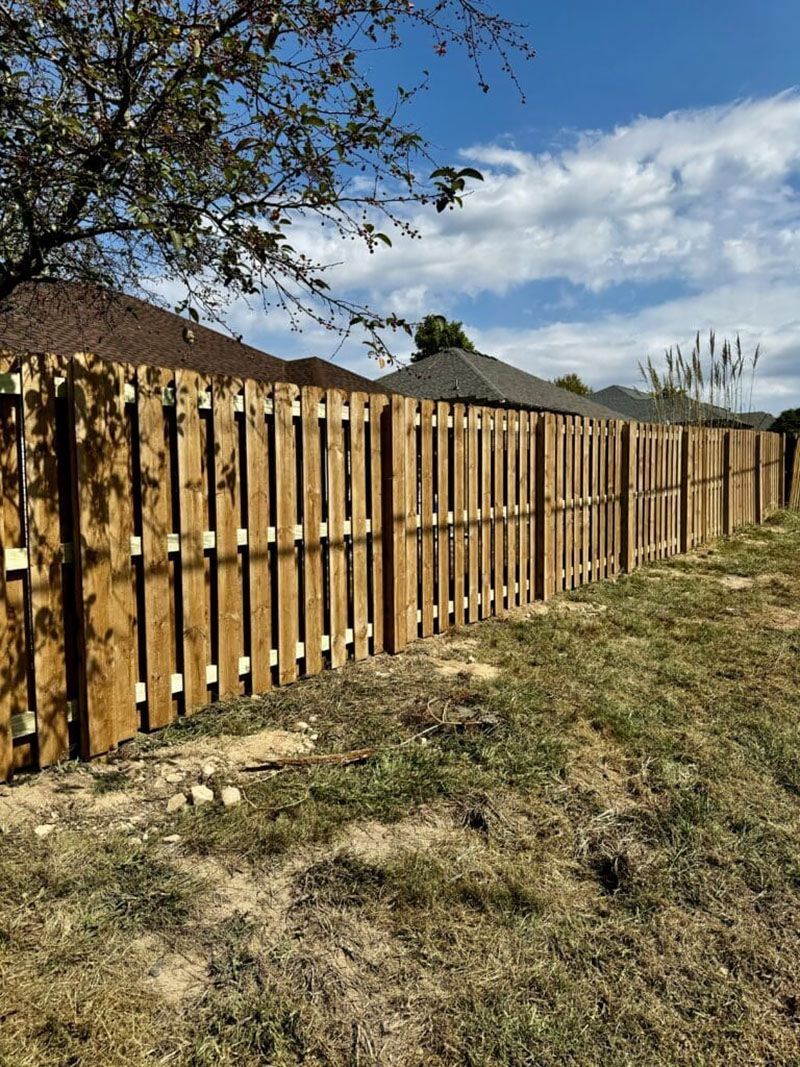 A wooden fence is sitting in the middle of a grassy field next to a house.
