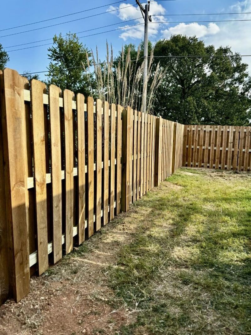 A wooden fence is surrounded by grass and trees in a yard.