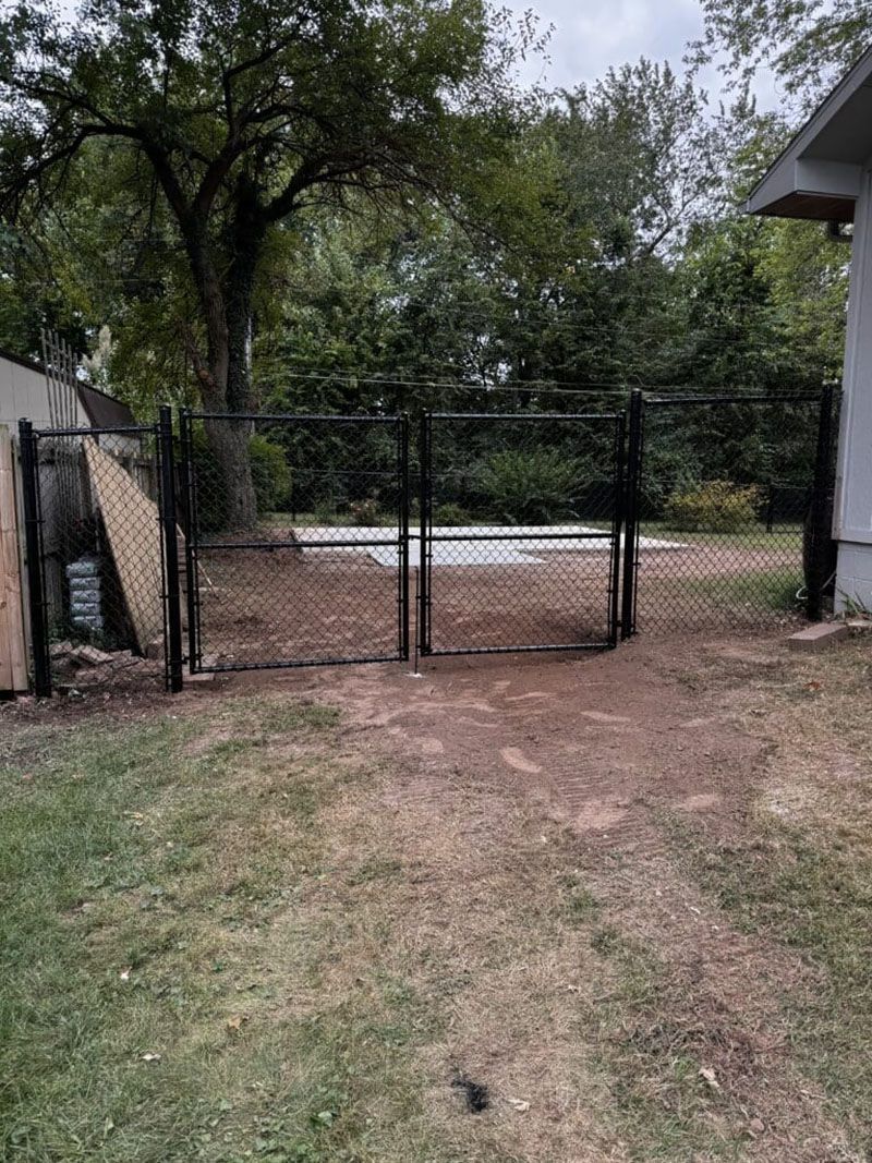 A chain link fence with a gate in the backyard of a house.