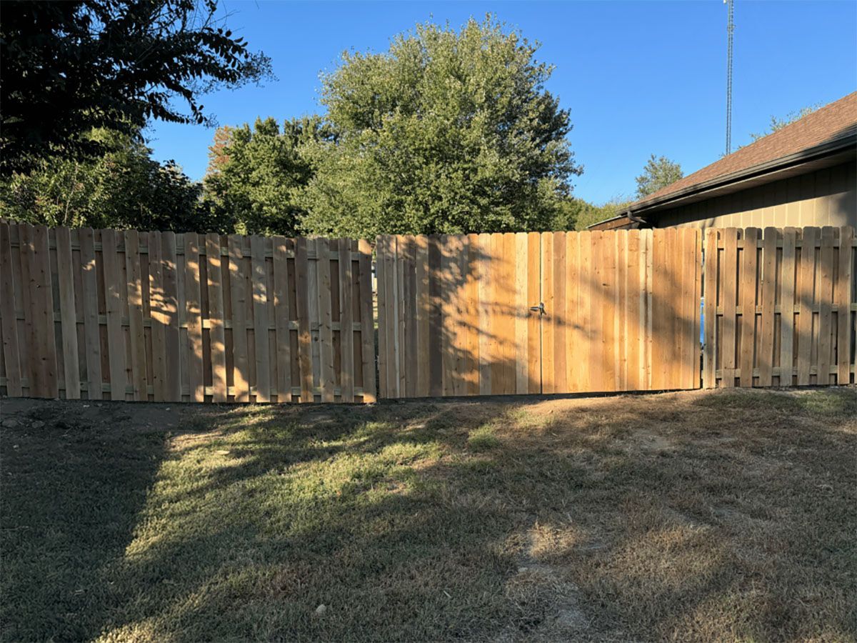 A wooden fence is sitting in the middle of a yard next to a house.