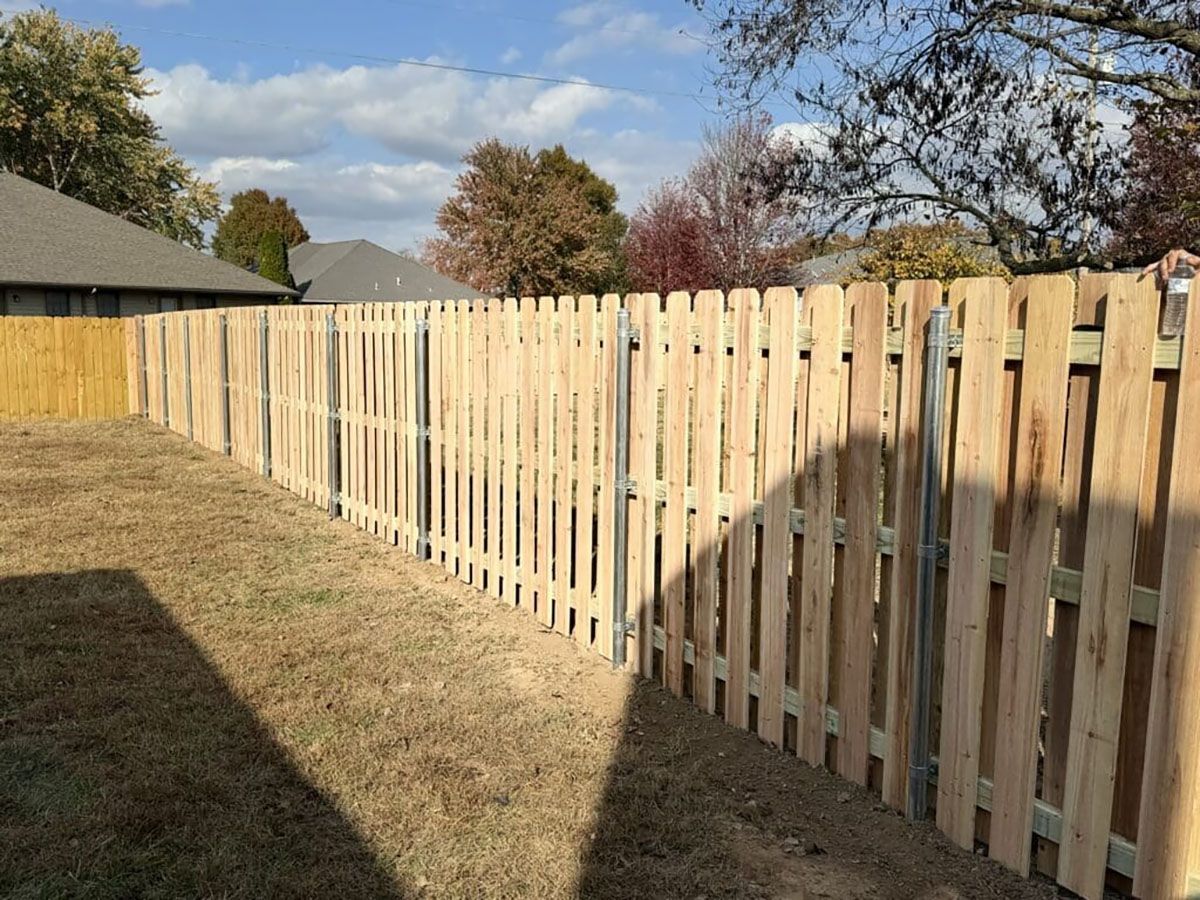 A wooden picket fence is in the backyard of a house.