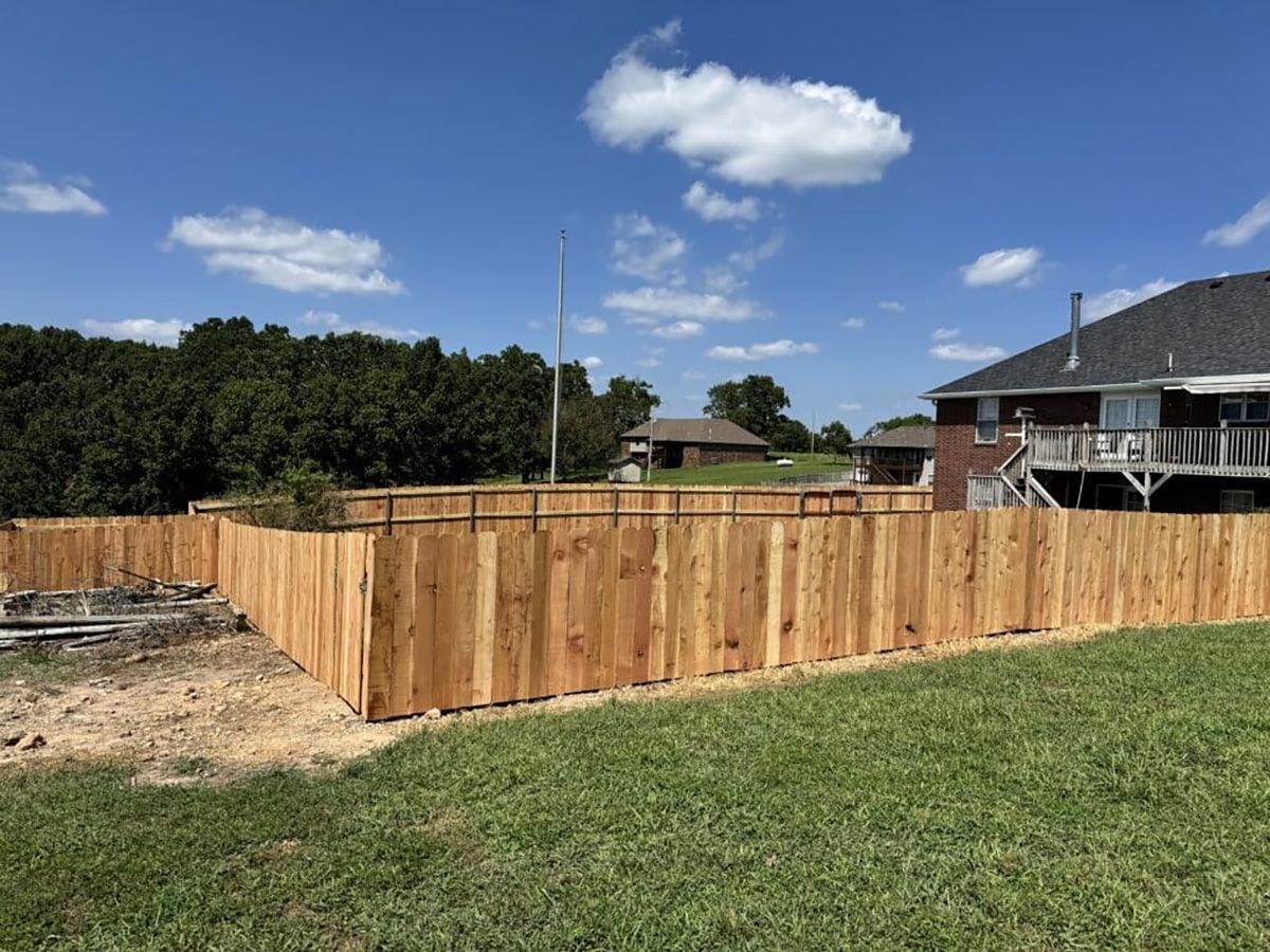 A wooden fence is in the middle of a lush green field in front of a house.