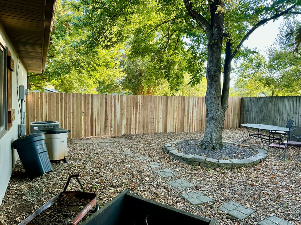 A backyard with a wooden fence and a tree.