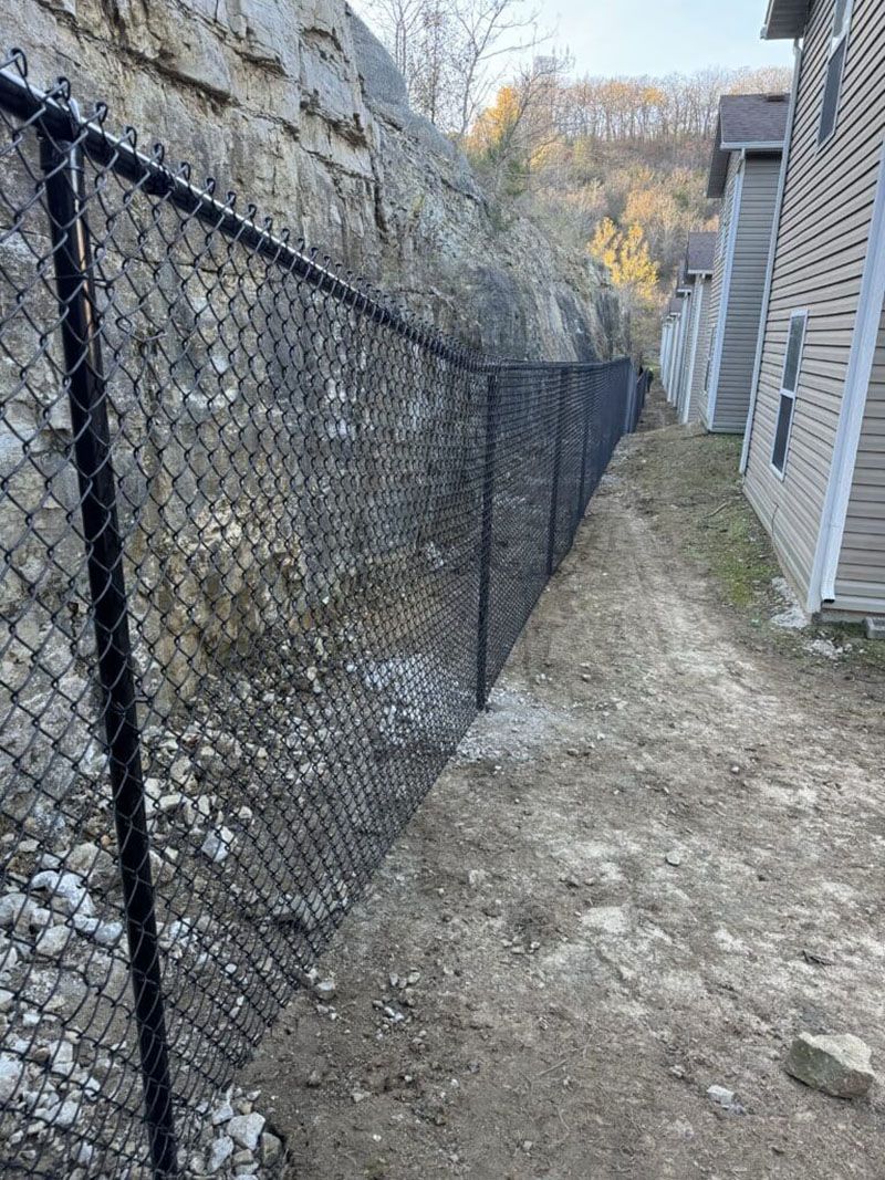 A chain link fence is surrounding a stone wall next to a house.